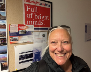Dr. Lynn Gibbard in front of a Fulbright sign that reads: Full of bright minds