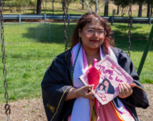 Arianna Bennett sits on a swing in graduation regalia holding her graduation cap.