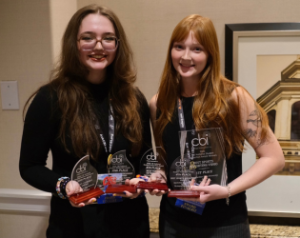 Two students stand next to each other wearing all black holding CBI trophies